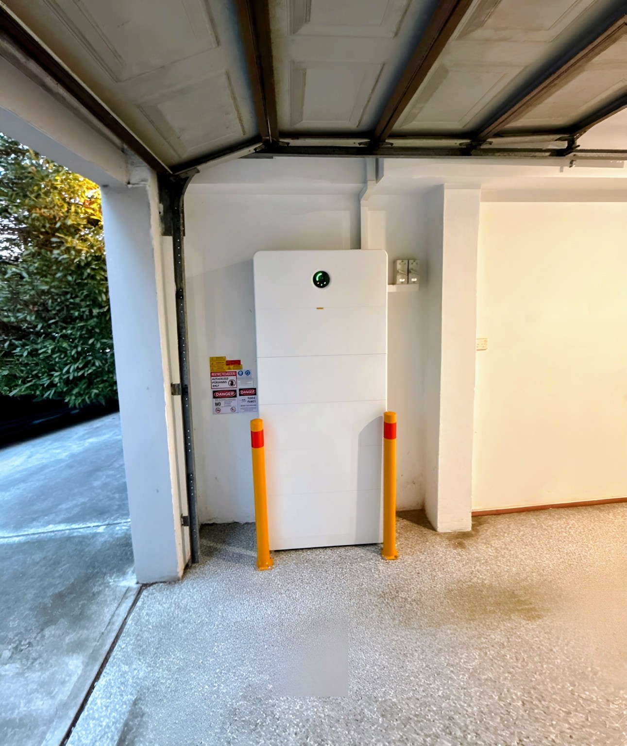 Completed Solar Paradigm home battery installation in a garage, with protective bollards and safety labels